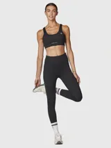 Top deportivo negro con escote redondo, tirantes anchos y un corte debajo del busto que crea una abertura. Incluye logo blanco en el pecho.