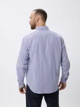 Camisa de manga larga con diseño de rayas finas verticales en azul y blanco, cuello clásico con botones y cierre frontal. Presenta un pequeño bordado en la pechera y puños abotonados.