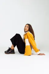 Camisa color mostaza de paño, corte oversize, con cuello clásico, cierre frontal con botones, mangas largas con puños abotonados y dos bolsillos de parche en el pecho.