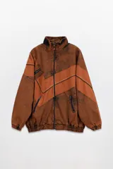 Campera olímpica de denim con efecto acid wash en tonos marrones y naranjas. Presenta un corte oversized con elástico en la cintura, cuello alto y cierre frontal. Posee bolsillos con cierre en la parte delantera y un parche con texto en el pecho.