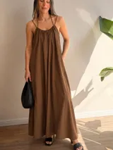 Vestido largo marrón de silueta amplia y caída fluida, con escote fruncido y tiritas finas ajustables al cuello.