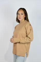 Buzo de punto color beige con cuello alto, mangas largas y detalle de botones decorativos en el hombro. Cuenta con aberturas laterales en el dobladillo.