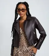 Campera estilo biker de material sintético (PU) color marrón oscuro, con cuello de solapa, cierre frontal de cremallera y bolsillos laterales con cremallera. Presenta detalles de broches a presión en las solapas y en los laterales inferiores.