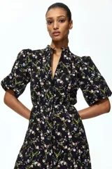 Vestido largo negro con estampado floreado, cuello mao, mangas globo cortas y falda escalonada con volados.