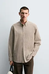 Camisa de algodón de manga larga, cuello abotonado y cierre frontal de botonadura. Presenta un patrón de cuadros pequeños en tonos beige, marrón y blanco.