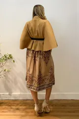 Capa corta negra de paño italiano con cuello alto y cinturón con hebilla dorada.