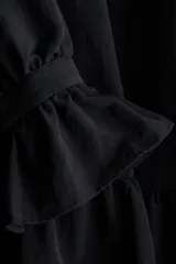 Vestido corto de corte holgado con cuello alto de volados y cierre frontal de botón. Presenta canesú fruncido, mangas largas abullonadas con puños acampanados y falda con costura fruncida en el bajo.