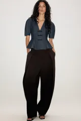 Blusa de denim oscuro con escote en pico, mangas cortas abullonadas y diseño peplum con bajo evasé. Presenta cierre frontal con alamares decorativos y cierre lateral con cremallera oculta.