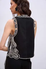 Blusa negra sin mangas, de corte recto y escote redondo, con detalles de bordados contrastantes en color blanco en los bordes y costados.