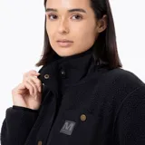 Campera polar sherpa de mujer en color negro, con cuello alto, cierre de botones a presión, bolsillos frontales con refuerzo en nylon y parche con logo de la marca en el pecho.