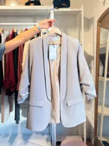 Blazer de corte sastre en color gris claro, con solapas clásicas, bolsillos frontales con solapa y mangas con detalle de frunce.