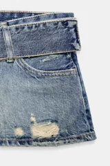 Shorts mini de tiro bajo confeccionados en denim azul con efecto desgastado y roturas. Presenta trabillas, bolsillos delanteros y un cinturón ancho integrado del mismo tejido con hebilla metálica.