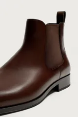 Bota Chelsea de hombre en color marrón oscuro, con diseño liso, punta afilada, elásticos laterales y tirador trasero.