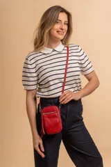 Bandolera porta celular color negro, confeccionada en símil cuero con textura granulada. Presenta un compartimento principal con cierre, un bolsillo frontal con cierre y detalle de borla decorativa, y correa regulable y desmontable.