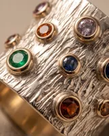 Anillo ancho de plata 925 con lámina de oro de 18k en los bordes, con textura estriada y engastes de circonias de colores.