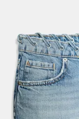Shorts de denim de tiro bajo y cinco bolsillos, con detalle de cordón entrelazado en la cintura del mismo tejido. Cuenta con cierre frontal con cremallera y botón metálico.