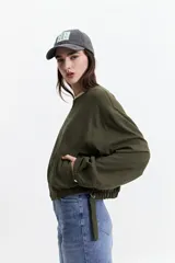 Campera verde militar sin cuello, con elástico y cinto regulable en la cintura, bolsillos amplios y cierre frontal.