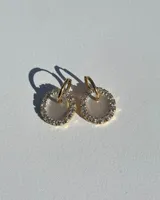 Aros dorados con dije circular de resina brillante color blanco y borde de strass. El arito es de acero quirúrgico.