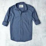 Camisa de vestir azul de algodón, con cuello clásico, cierre frontal con botones, mangas largas con puños abotonados y logo bordado en el pecho.