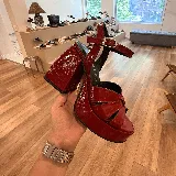 Sandalias de plataforma color rojo charol, con tiras cruzadas en el empeine, pulsera al tobillo con hebilla metálica y tacón cuadrado.