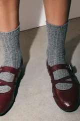 Bailarinas color bordó con efecto acharolado, detalle de pespuntes, cierre de hebilla metálica ajustable y tiras elásticas cruzadas en la parte frontal. Acabado en punta redonda y suela de 0,5 cm.