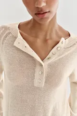 Jersey de punto color beige, con cuello redondo y cierre frontal parcial de botones, manga larga y acabados en rib.