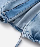 Campera tipo bomber confeccionada en tejido de jean, con cierre frontal de cremallera, capucha ajustable con cordones y bolsillos frontales. Presenta puños y cintura elásticos, ofreciendo un ajuste cómodo y un estilo urbano.