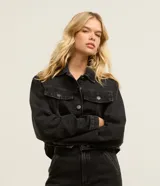Campera de jean color negro, de corte regular y largo corto, con cuello inglés, mangas largas, cierre frontal con botones metálicos y bolsillos con solapa en el pecho.