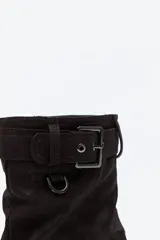 Bota de caña media color negro, con suela robusta dentada y detalle de hebilla ajustable en la parte superior. Presenta una argolla metálica lateral y un diseño de estética urbana con acabado texturizado.