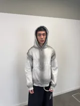 Buzo con capucha y cierre frontal, color gris con efecto lavado degradado. Presenta estampado gráfico en color blanco que recorre el pecho y las mangas, bolsillos laterales y etiqueta de marca en el puño.