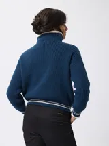 Sweater de tejido grueso en color beige, con cuello alto y cierre frontal parcial. Presenta detalles de rayas negras en contraste en el borde del cuello y en los puños.