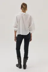 Blusa blanca con lunares en relieve, cuello con volados y lazos, mangas abullonadas 3/4 y bordados con lentejuelas en el frente.