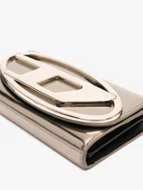 Cartera Diesel tipo sobre, color dorado metalizado, con logo ovalado en relieve. Incluye correa desmontable para usar como bandolera.