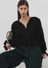 Blusa de algodón negra con detalles florales bordados, cuello en pico con cierre de lazo, manga larga abullonada y diseño recto con vuelo en la cintura.