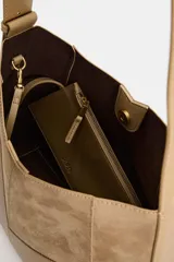 Bolso de hombro color tostado con diseño estructurado que combina paneles de cuero liso y gamuza con pespuntes visibles. Cuenta con un asa larga de hombro ajustable y cierre superior con botón imantado.