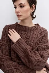 Sweater de punto color blanco off-white, con cuello redondo y diseño texturizado con trenzas y pompones en el frente.