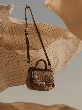 Cartera de mano y bandolera de cuero vacuno en color marrón, con solapa frontal texturizada, cierre metálico giratorio y correa larga ajustable y extraíble.