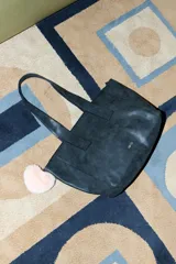Cartera tipo shopper de cuero vegano con acabado efecto gastado en color marrón oscuro. Cuenta con doble asa de hombro y un charm colgante de pompón de peluche en color rosado.