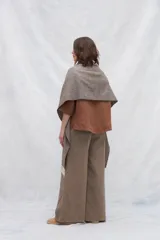 Chal de lana fina sin teñir con diseño de cuadros sutiles, cierre frontal con alamar y bolsillos de cuero metalizado. Presenta terminaciones con flecos en el ruedo y un calce estructurado en los hombros.