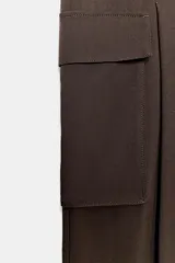 Pantalón cargo de tiro medio en color marrón oscuro, con corte recto y amplio. Presenta bolsillos laterales tipo cargo con solapa y detalle de pliegues frontales. Cierre frontal con cremallera y botón.
