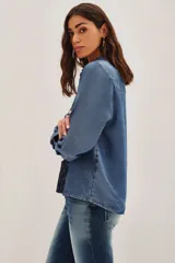Camisa de denim azul con bordados negros en el frente, de manga larga, cuello clásico y cierre frontal con botones.