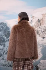 Chaqueta de pelo sintético color marrón chocolate, con cuello alto y cierre frontal mediante cremallera.