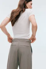 Pantalón sastre de tiro alto, color gris, con cordón ajustable en la cintura, piernas amplias con pinzas, raya marcada, bolsillos laterales discretos y bolsillos insertados atrás.