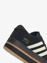 Zapatillas Adidas Gazelle Stack para mujer, color negro con las tres tiras laterales en blanco y suela de plataforma en color caramelo.