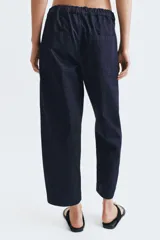 Pantalón de jean azul oscuro de tiro medio, con corte holgado y diseño de pierna ancha. Presenta cintura elástica en la parte posterior, cierre frontal con cremallera y botón metálico, y bolsillos de plastrón en el delantero.