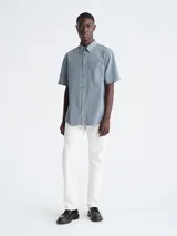 Camisa celeste de manga corta, con cuello clásico, cierre frontal con botones, bolsillo en el pecho con logo bordado de la marca Calvin Klein y corte holgado.