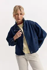 Campera de jean color negro, de calce amplio y largo a la cintura, con cuello alto y cierre frontal con broches a presión.