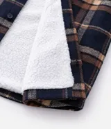 Campera tipo trucker de franela con estampado de cuadros, cuello inglés, cierre frontal con botones, bolsillos con solapa en el pecho y bolsillos laterales. Cuenta con forro interno de sherpa para mayor calidez.