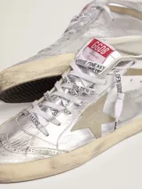 Zapatilla de caña media inspirada en el estilo skate de los ochenta, confeccionada en cuero vacuno plateado con efecto envejecido, estrella lateral y detalles en gamuza beige. Incorpora perforaciones de estilo inglés, cordones blancos con logotipo y suela de goma con acabado desgastado.