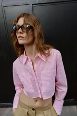 Camisa corta rosa con rayas verticales finas, cuello solapa, manga larga y bolsillos delanteros de plastrón. Cierre frontal con botones ocultos.